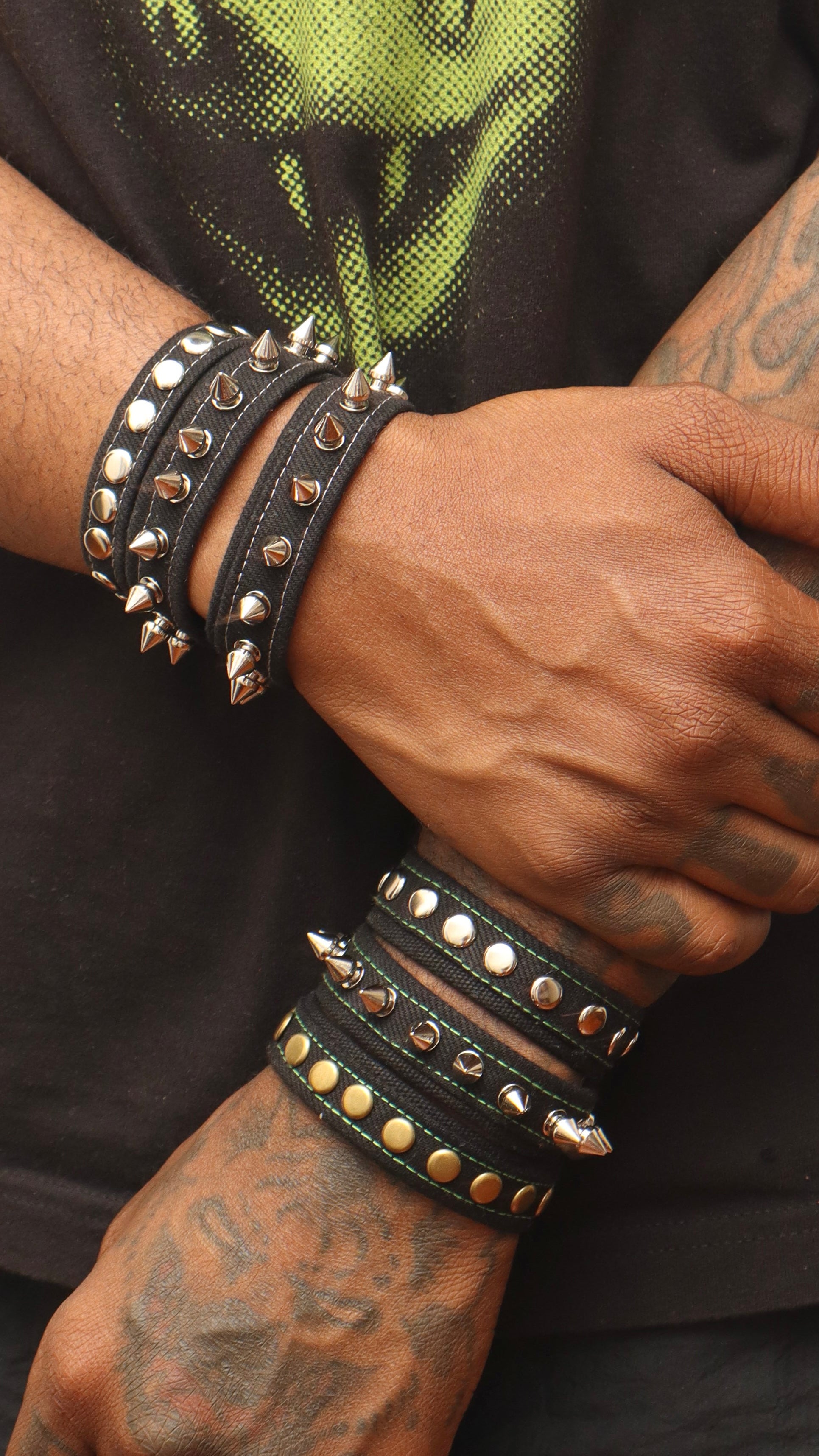 Close-up of a person's arm wearing multiple studded bracelets on a dark background