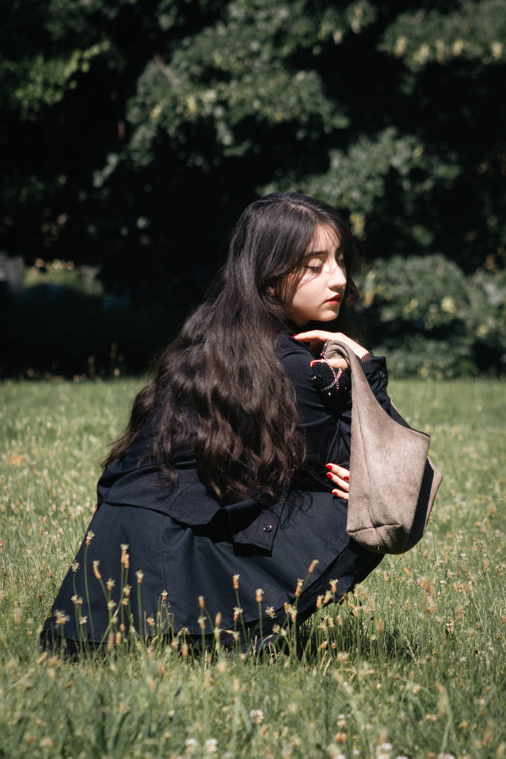 Person sitting on grass holding a suede bag in a natural setting
