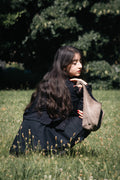 Person sitting on grass holding a suede bag in a natural setting