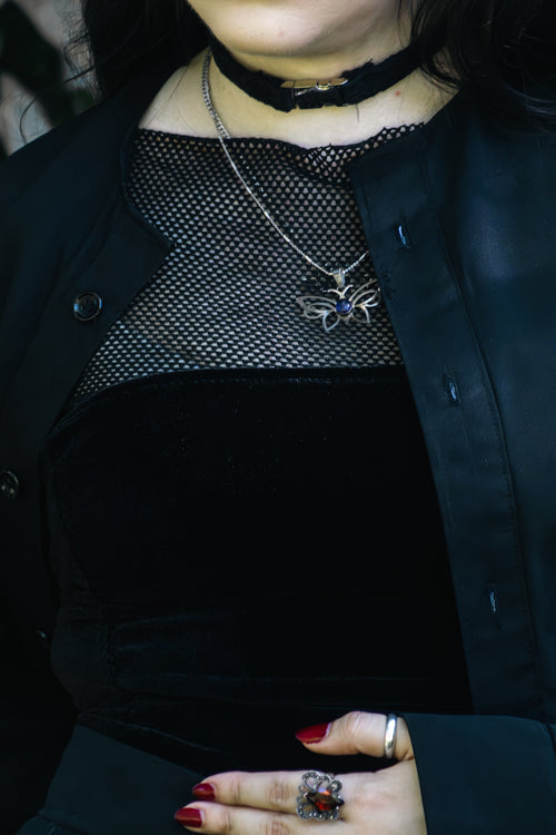 Person wearing a black coat with a spider necklace and red nail polish.