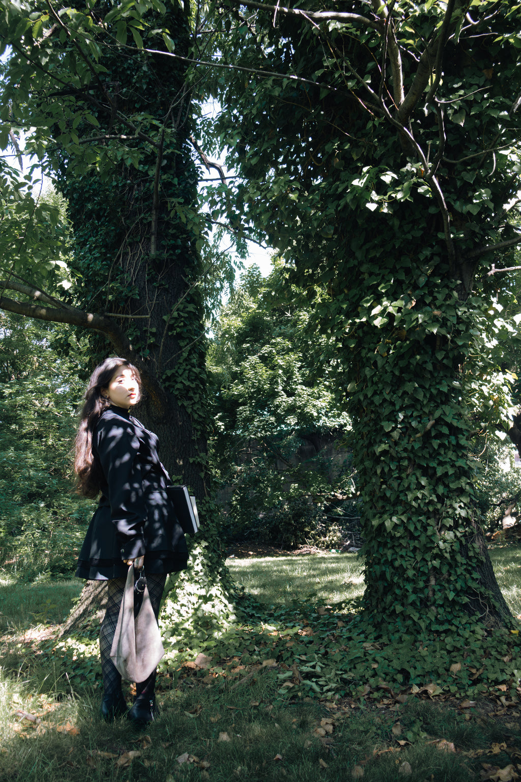Person standing between two large trees covered in green ivy in a forest.