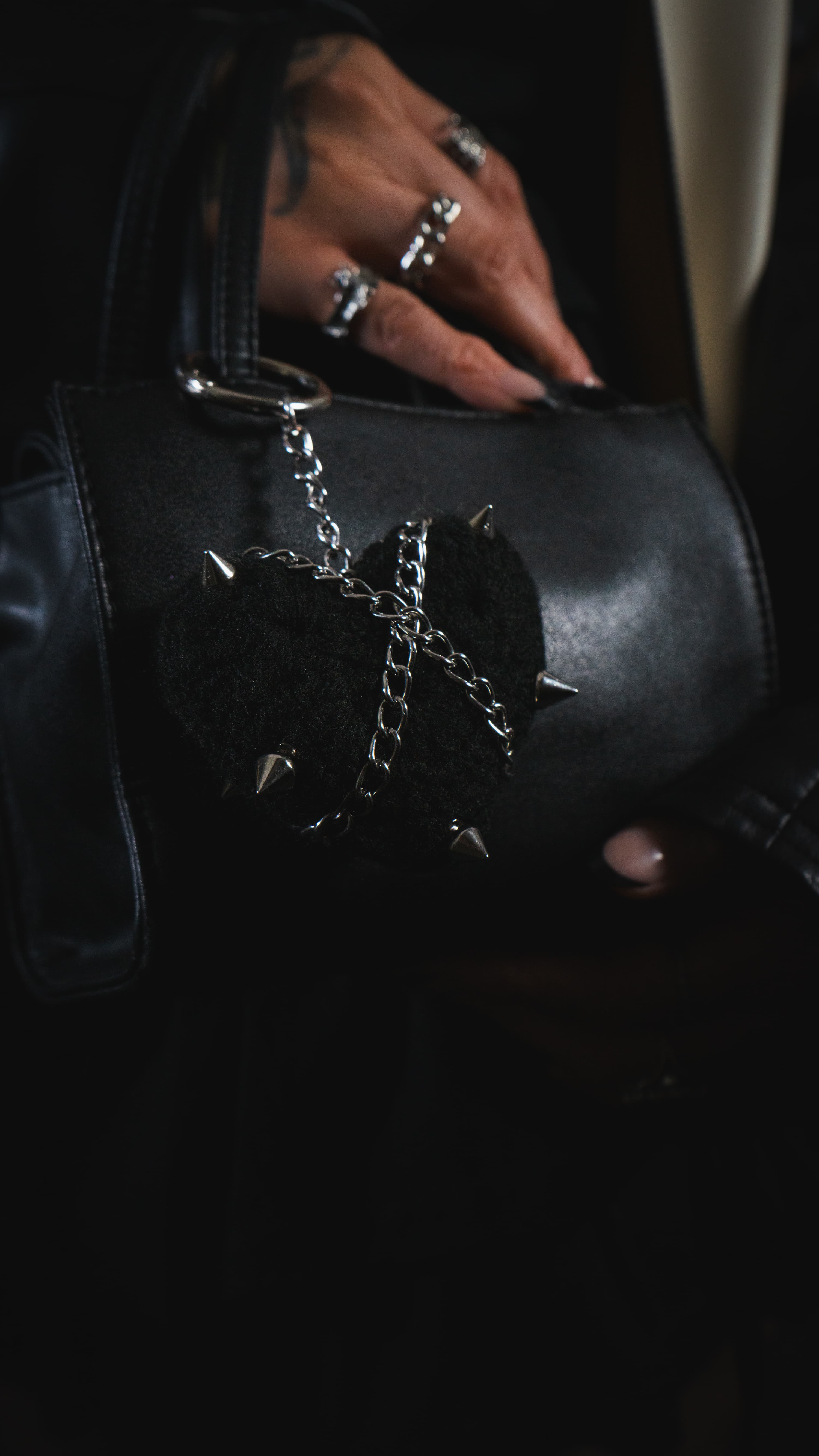 Hand holding the CUTIES Black Metal Bag Charm attached to a black leather bag, highlighting the metal chain and spiked detailing