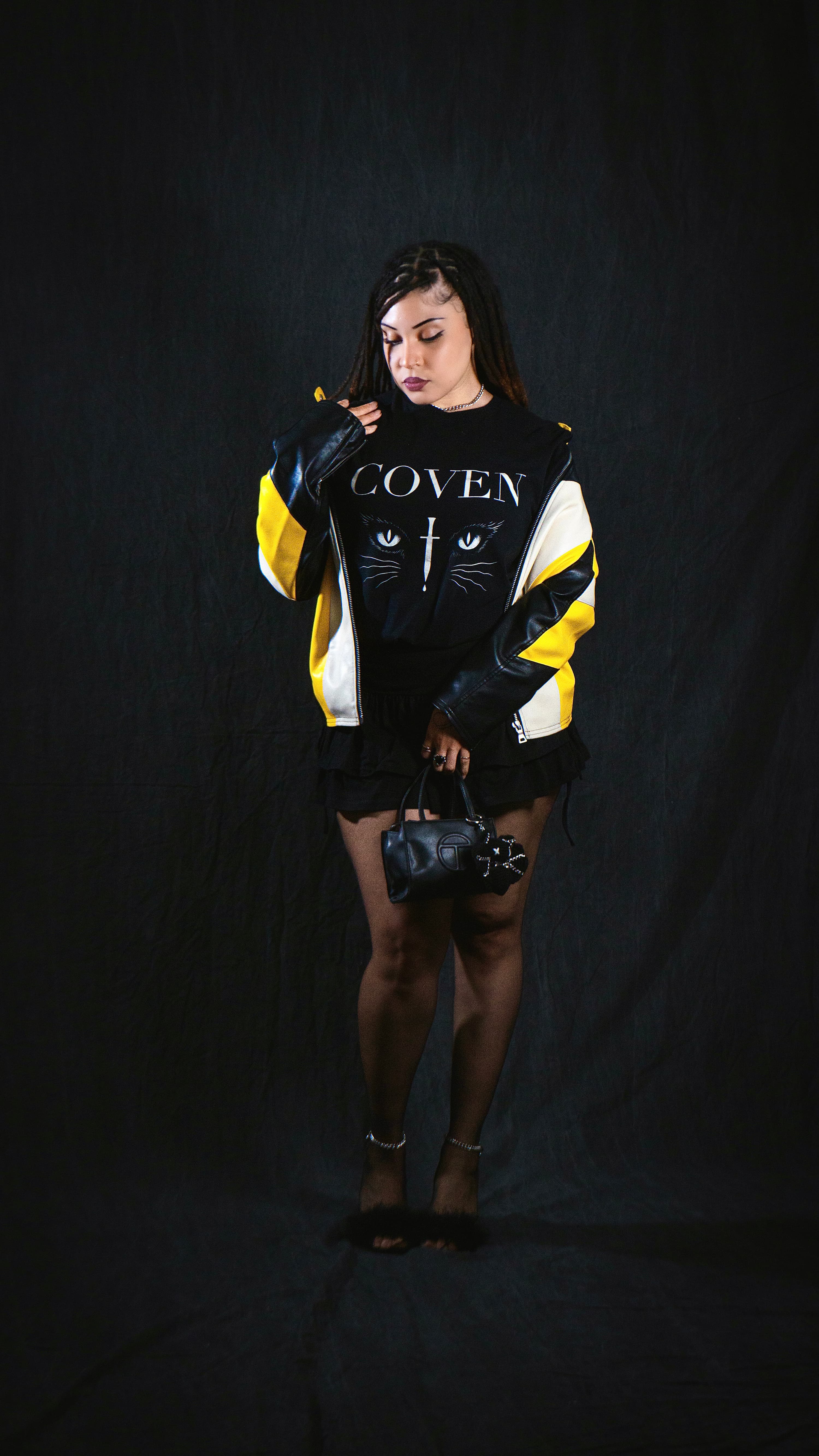 Person wearing a black 'COVEN' shirt with cat designs on a dark background