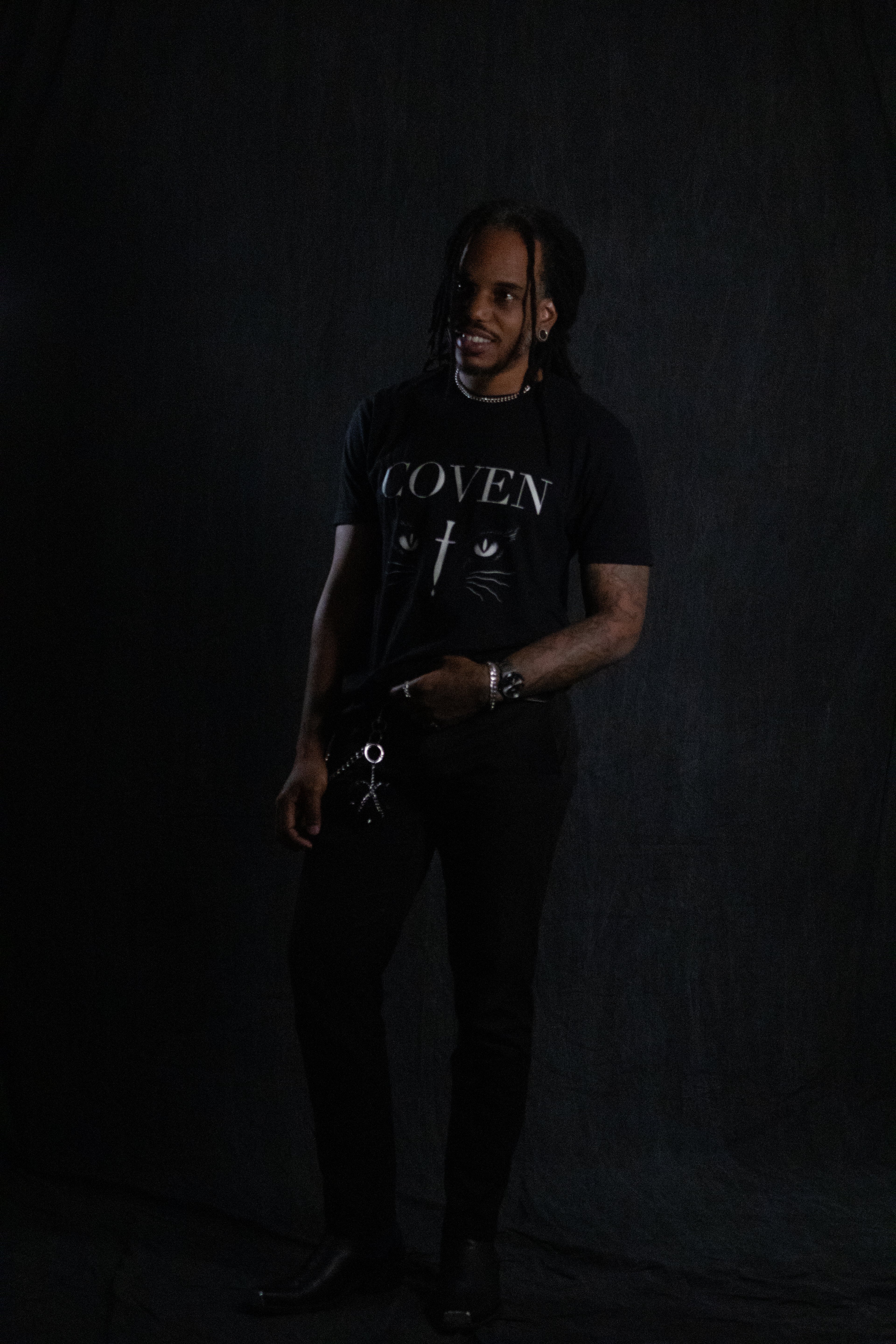 Person wearing a black t-shirt with 'COVEN' text against a dark background