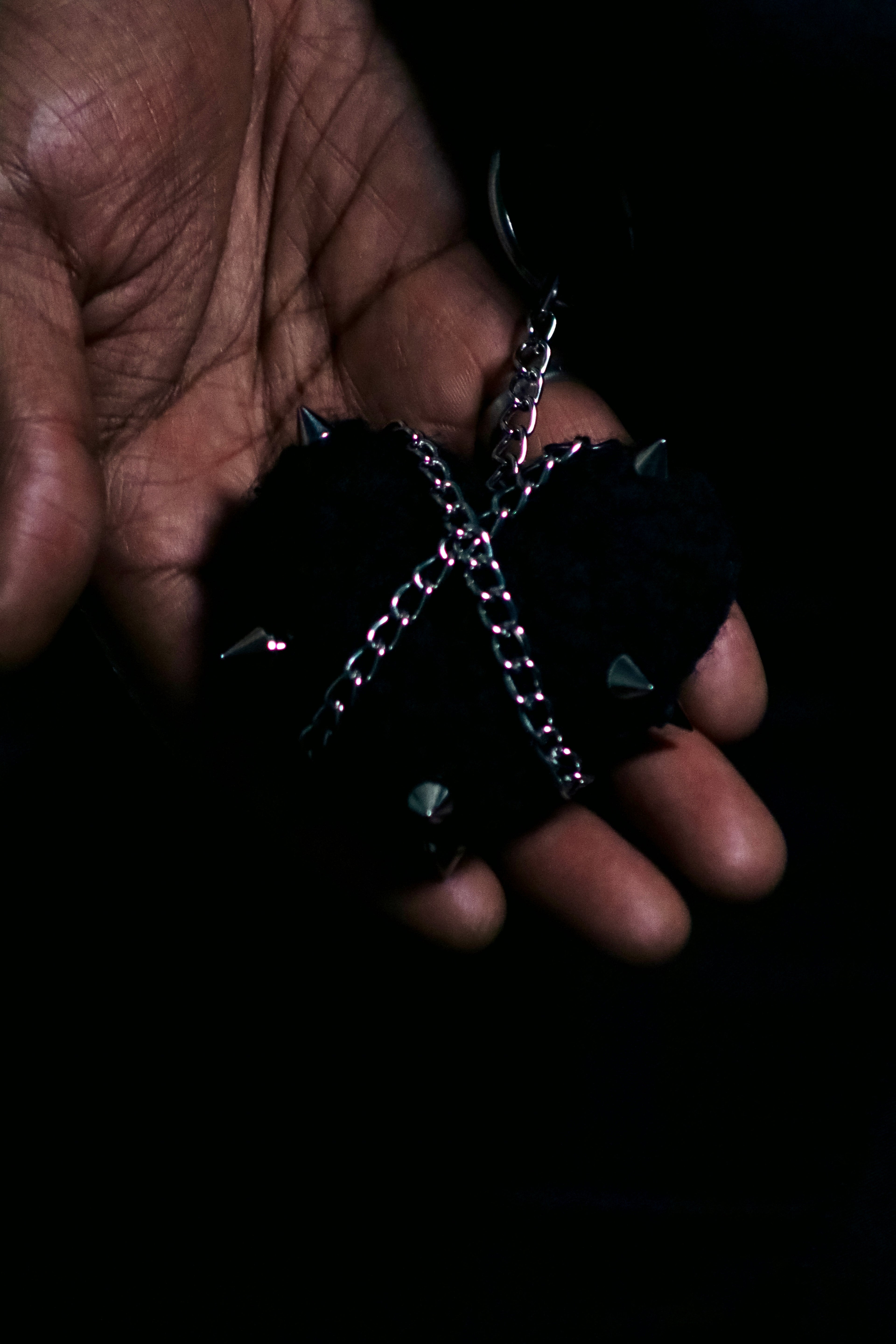 Close-up of the CUTIES Black Metal Bag Charm resting in a hand, showing the plush texture, spikes, and chain hardware